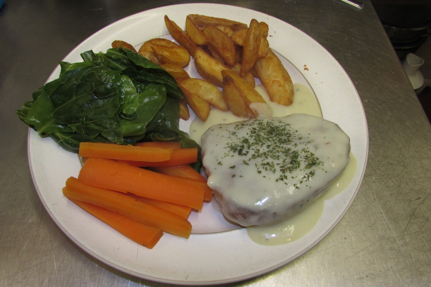 A main with a creamy sauce, carrots, greens and potato wedges